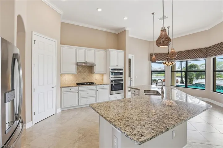 Kitchen with appliances with stainless steel finishes, a center island with sink, decorative light fixtures, light stone counters, and white cabinetry