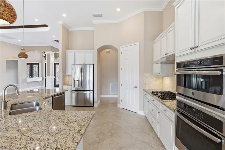 Kitchen with appliances with stainless steel finishes, arched walkways, white cabinetry, ornamental molding, and light stone counters