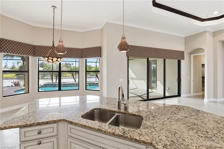 Kitchen with hanging light fixtures, light tile patterned floors, light stone counters, crown molding, and white cabinetry