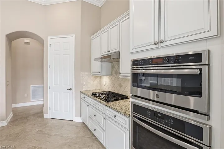 Kitchen with decorative backsplash, light stone counters, white cabinets, ornamental molding, and arched walkways