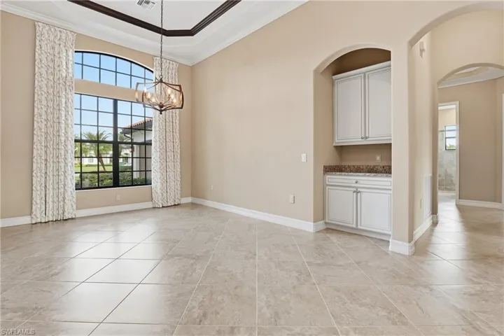 Unfurnished dining area featuring crown molding, a chandelier, arched walkways, a raised ceiling, and light tile patterned floors