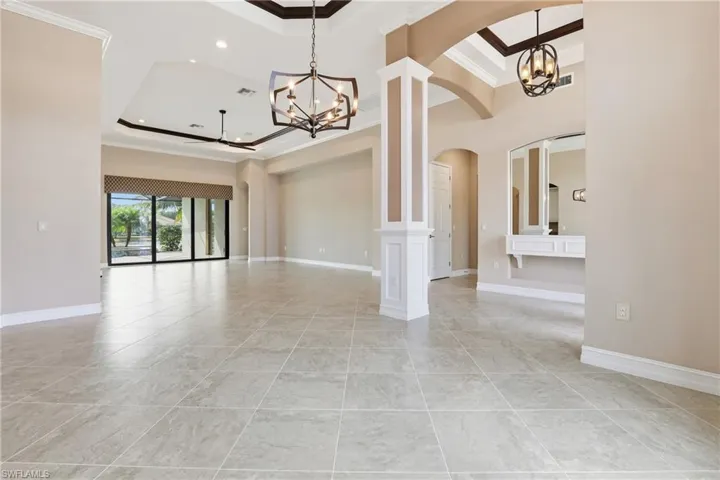 Empty room with ornamental molding, a tray ceiling, a chandelier, arched walkways, and decorative columns
