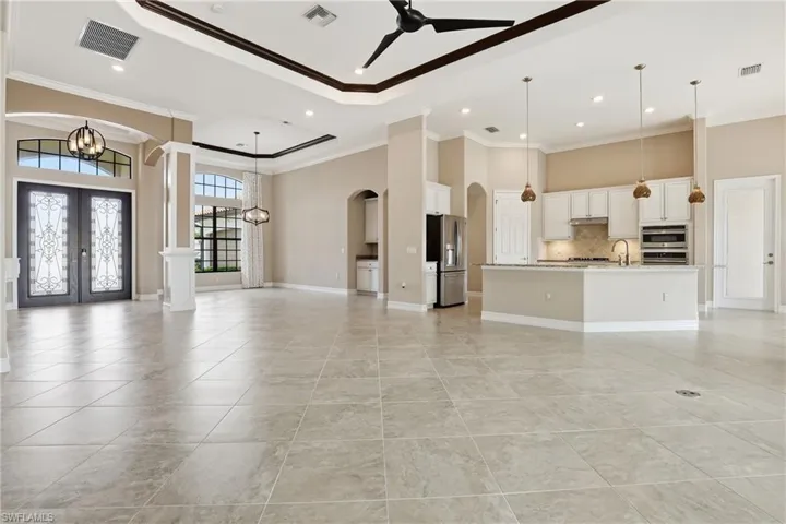 Unfurnished living room featuring ceiling fan, a high ceiling, french doors, ornamental molding, and arched walkways