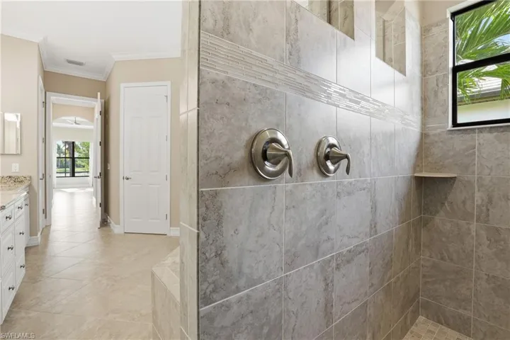 Bathroom featuring vanity, ornamental molding, light tile patterned flooring, and a tile shower