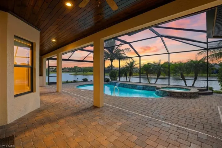 Pool at dusk featuring a patio area, glass enclosure, a pool with connected hot tub, a sunroom, and a water view