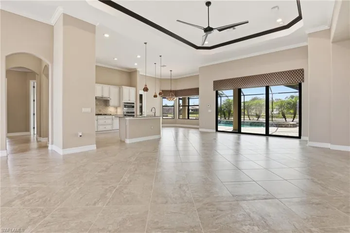 Unfurnished living room with arched walkways, crown molding, recessed lighting, a high ceiling, and a ceiling fan