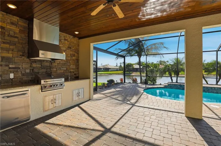 Outdoor pool featuring exterior kitchen, a patio area, a sunroom, a water view, and glass enclosure