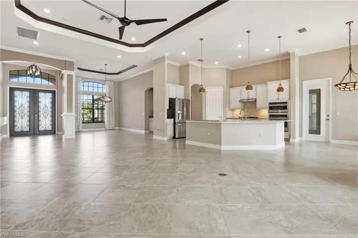 Unfurnished living room with french doors, a chandelier, ornamental molding, arched walkways, and a ceiling fan