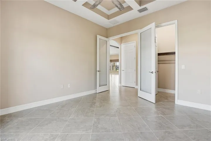 Unfurnished bedroom with french doors, a walk in closet, and coffered ceiling