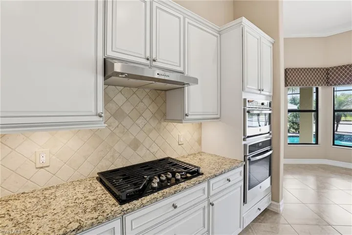 Kitchen featuring white cabinets, under cabinet range hood, black gas cooktop, light stone counters, and ornamental molding