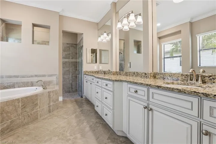 Bathroom featuring a garden tub, double vanity, ornamental molding, and a stall shower