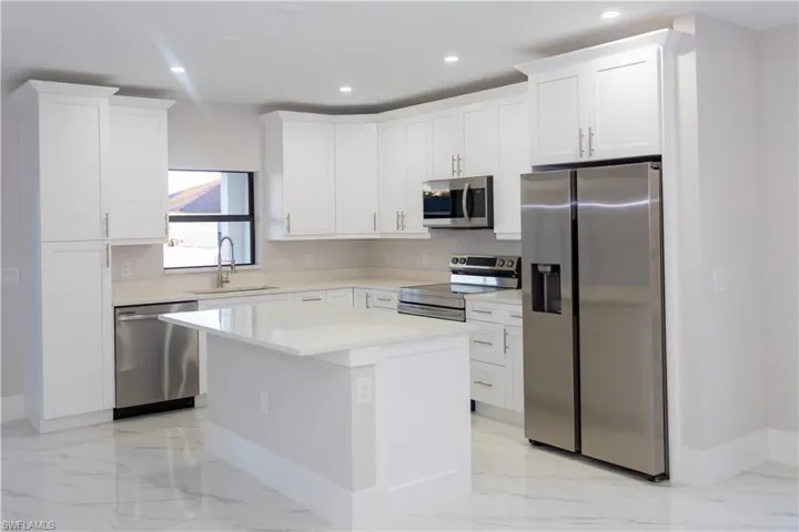 Kitchen with stainless steel appliances, white cabinets, a center island, light stone counters, and recessed lighting