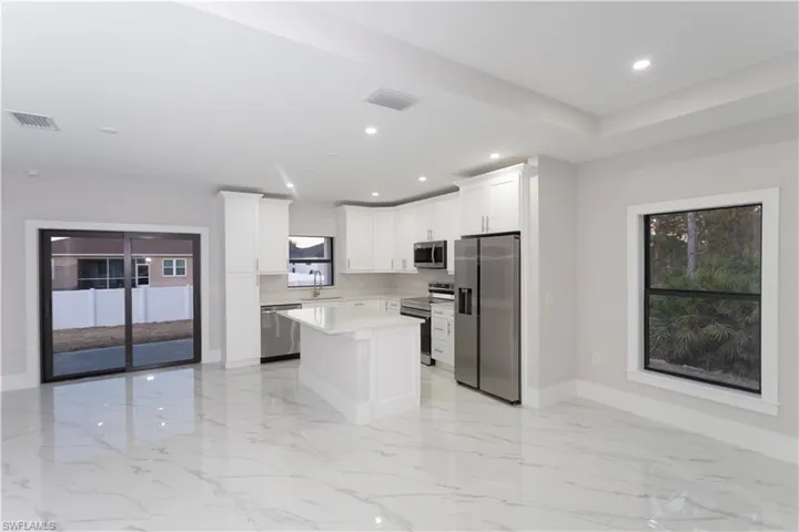 Kitchen with stainless steel appliances, a center island, white cabinets, recessed lighting, and light stone counters