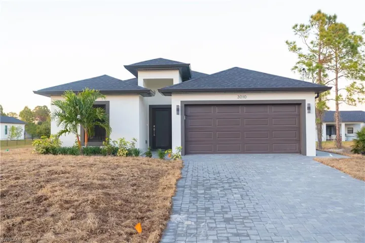 View of front facade featuring decorative driveway, stucco siding, a garage, and roof with shingles