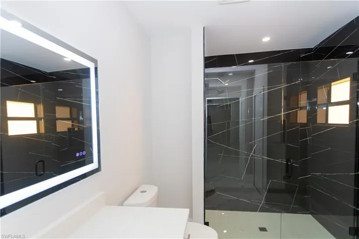 Bathroom with vanity, a marble finish shower, and recessed lighting