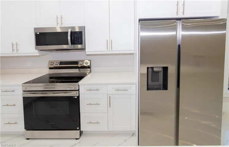 Kitchen featuring stainless steel appliances, white cabinets, and light stone counters