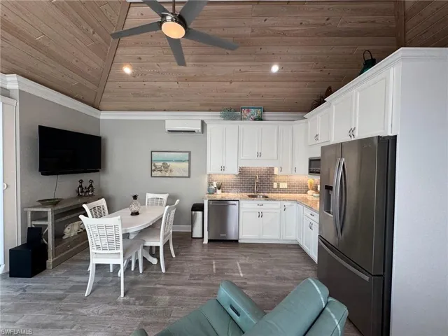 Kitchen with a wall mounted air conditioner, stainless steel appliances, white cabinets, dark wood-type flooring, and ornamental molding