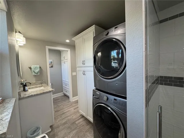 Clothes washing area featuring sink, stacked washer / drying machine, and light wood-type flooring
