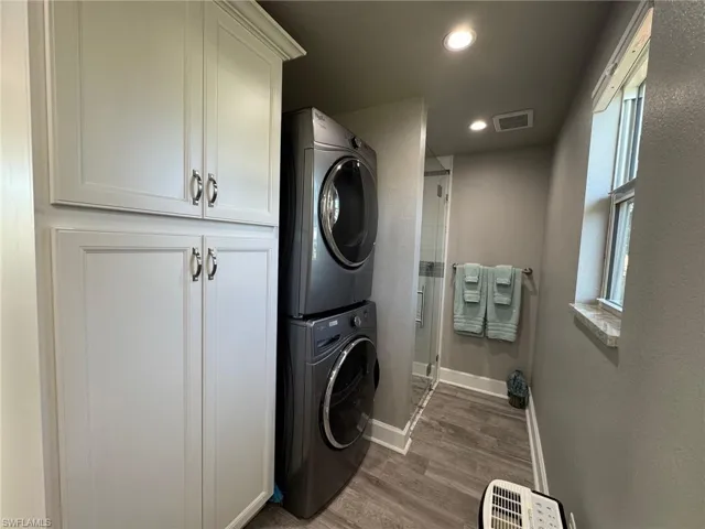 Laundry room with cabinets, hardwood / wood-style floors, and stacked washing maching and dryer
