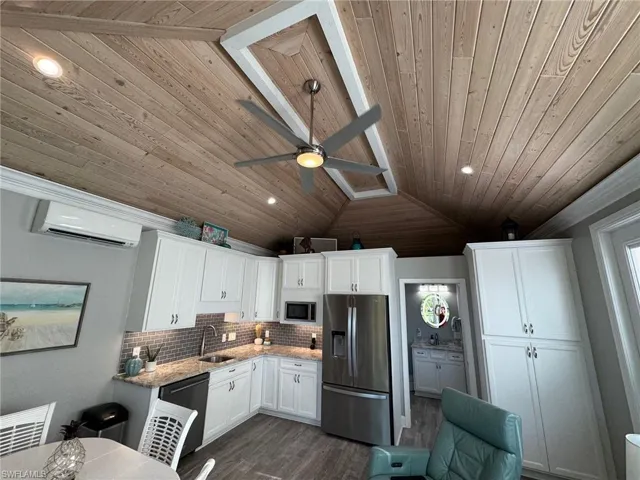 Kitchen featuring stainless steel appliances, lofted ceiling, white cabinets, light stone counters, and a wall mounted AC
