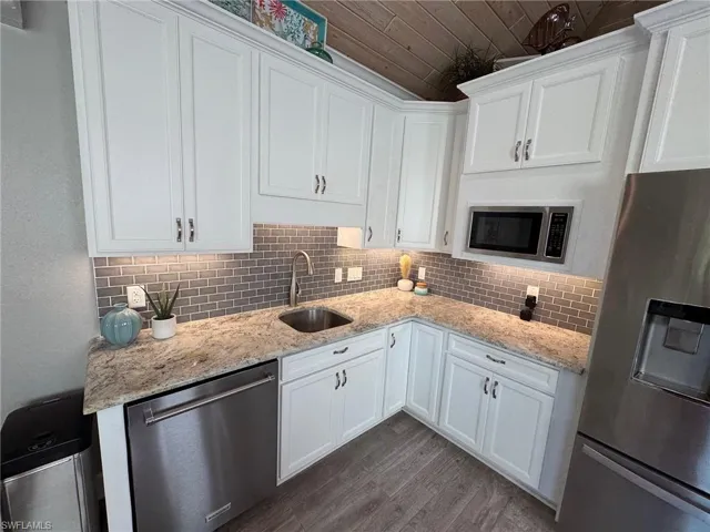 Kitchen with sink, appliances with stainless steel finishes, wood-type flooring, and white cabinetry