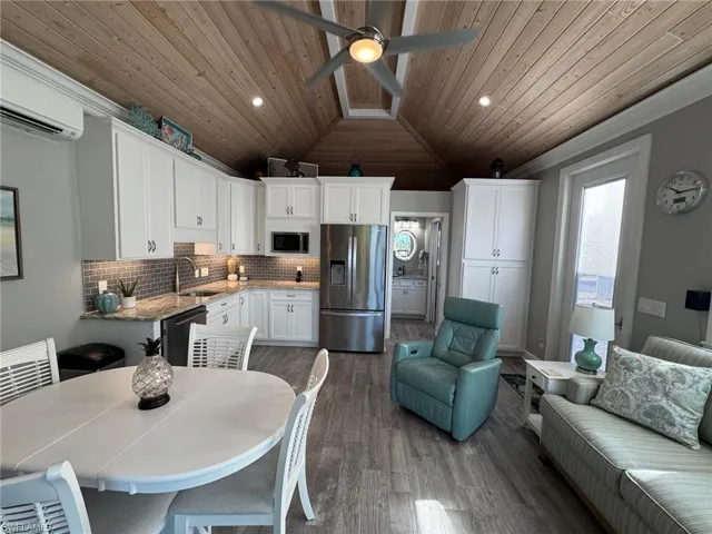 Kitchen with a wall unit AC, lofted ceiling, white cabinets, sink, and stainless steel appliances