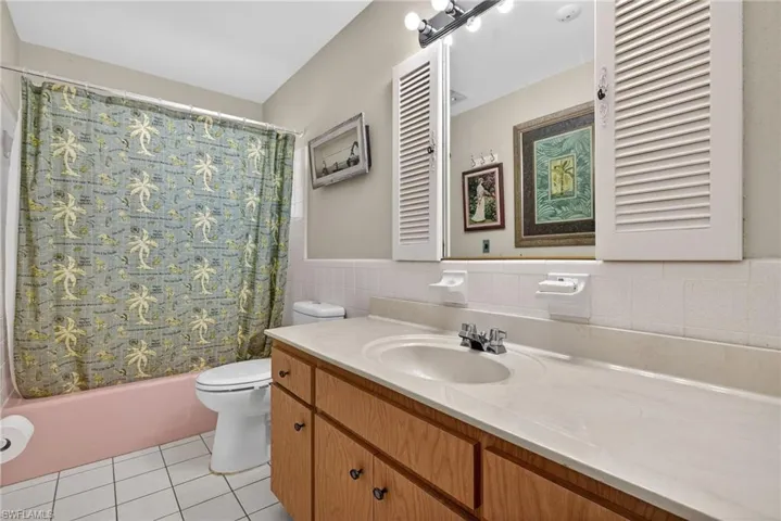 Bathroom featuring vanity, shower / bathtub combination with curtain, tile walls, light tile patterned floors, and wainscoting