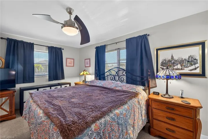 Carpeted bedroom featuring multiple windows and ceiling fan