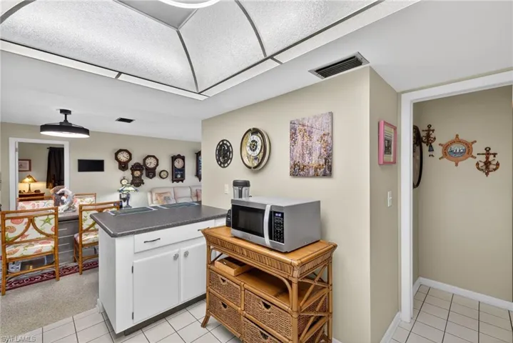 Kitchen featuring stainless steel microwave, white cabinetry, dark countertops, light tile patterned flooring, and a peninsula