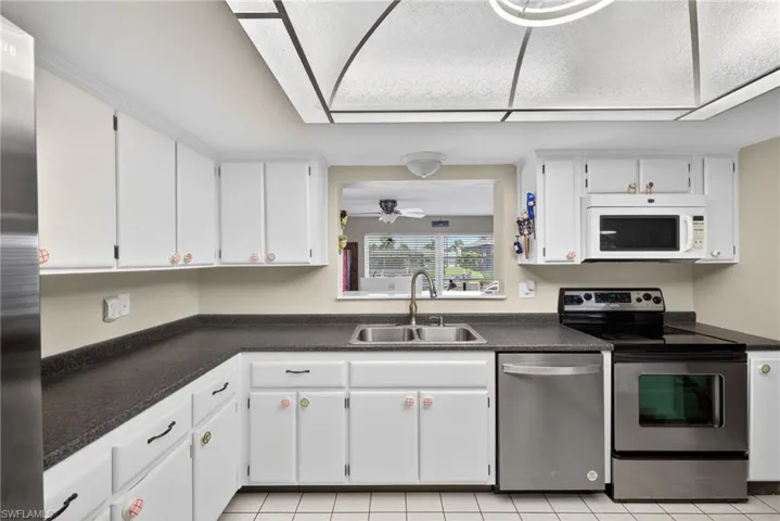 Kitchen featuring stainless steel appliances, dark countertops, white cabinets, ceiling fan, and light tile patterned floors
