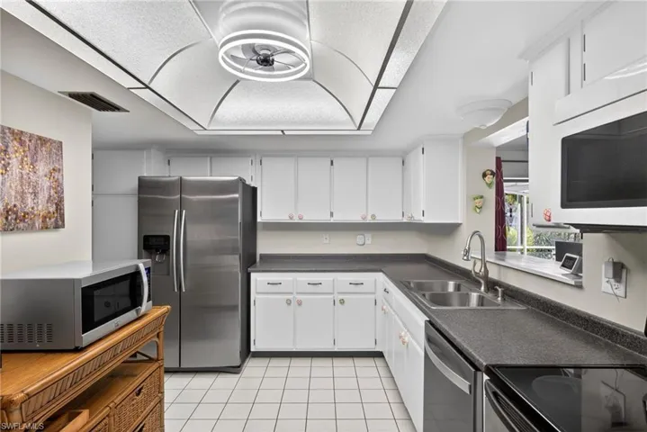 Kitchen featuring dark countertops, stainless steel appliances, white cabinets, and light tile patterned floors