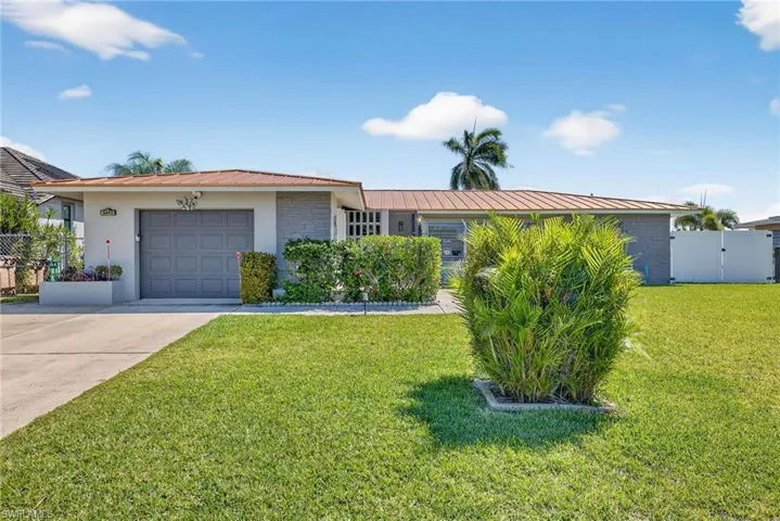 Ranch-style home featuring an attached garage, a gate, driveway, a metal roof, and stucco siding