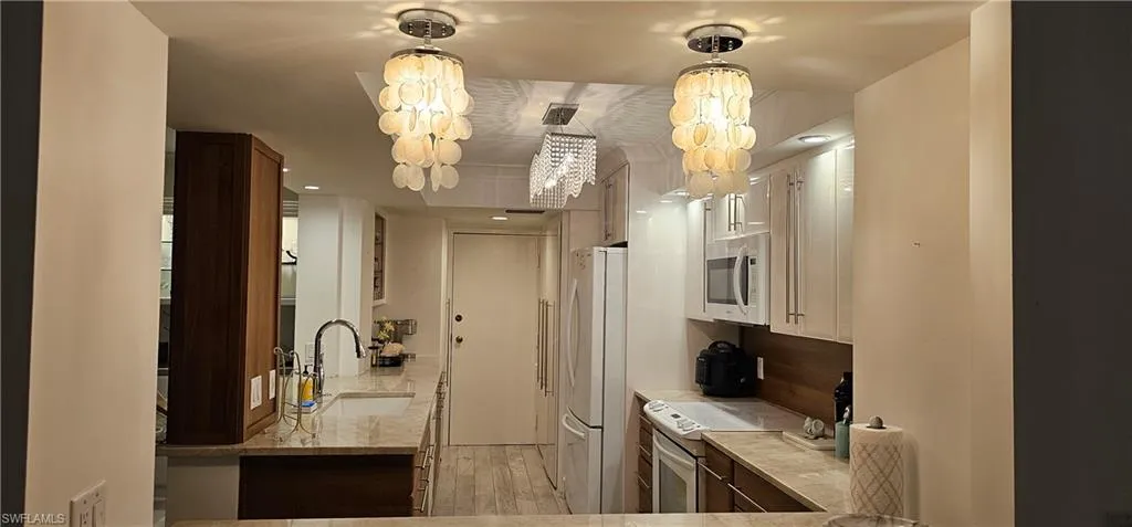 Kitchen featuring white appliances, light wood-style floors, decorative light fixtures, and light stone countertops