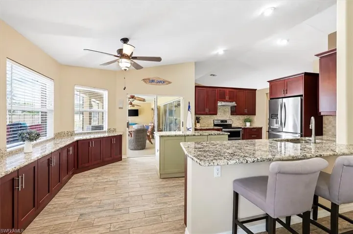 Kitchen featuring wood-finish flooring, granite countertops, stainless steel appliances, dark wood cabinetry, and a center island with a light-toned base