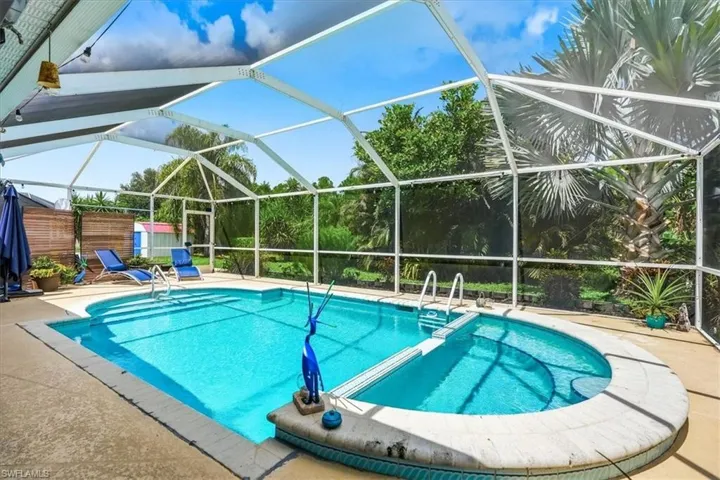 Screened-in outdoor pool featuring a curved spa, integrated steps, and surrounding concrete decking