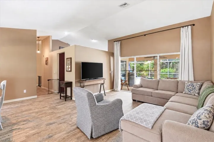 Vaulted ceilings, wood-finish flooring, sliding glass doors to outdoor area, and a contemporary wall-mounted light fixture