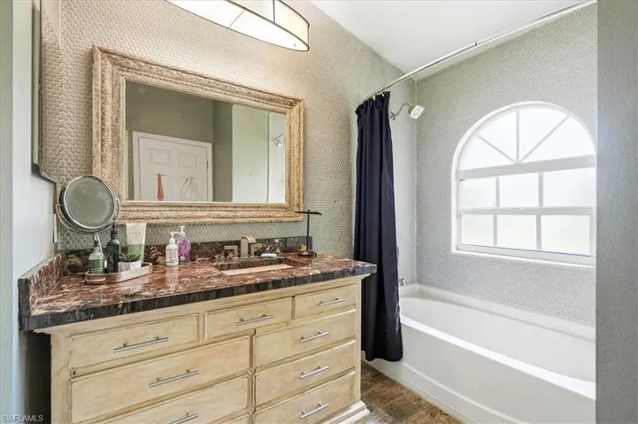 Arched window, built-in bathtub, vanity with a dark countertop, large framed mirror, and wall-mounted light fixture