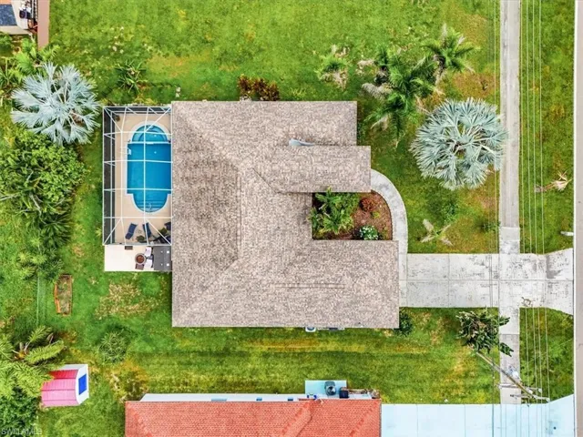 Screened swimming pool with a curved design, expansive green lawn, mature palm trees, concrete driveway, and established landscaping