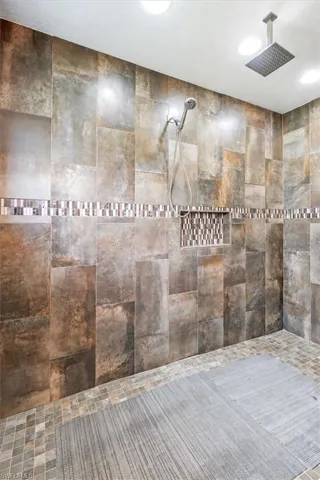 Tiled shower with handheld shower fixture, rain shower head, recessed lighting, mosaic tile accent, and built-in tile niche
