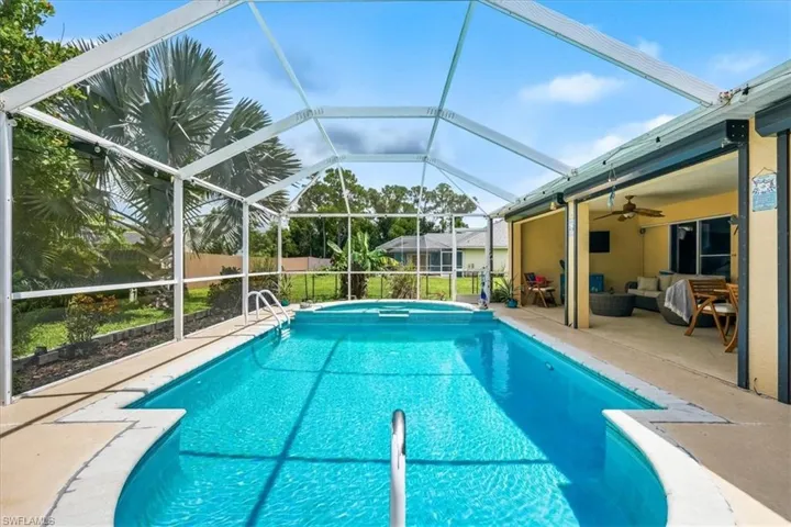 Screened enclosure featuring a swimming pool, integrated spa, and concrete decking