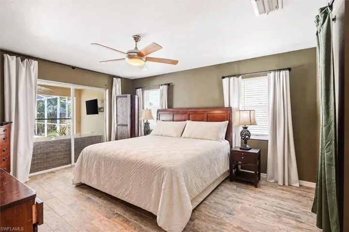 Wood-finish flooring, ceiling fan with integrated lighting, multiple windows, and a sliding glass door