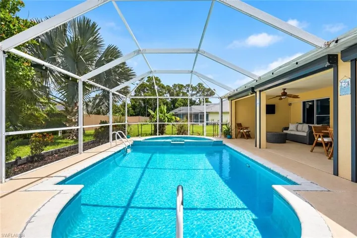 Screened-in swimming pool with an integrated spa, expansive pool deck, and a covered lanai featuring a ceiling fan