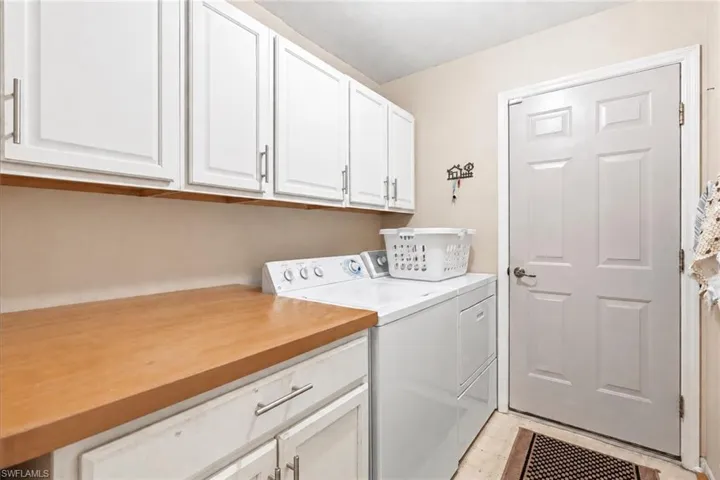 White shaker-style upper cabinetry with brushed nickel hardware, light wood-finish countertop, white paneled door, and durable flooring