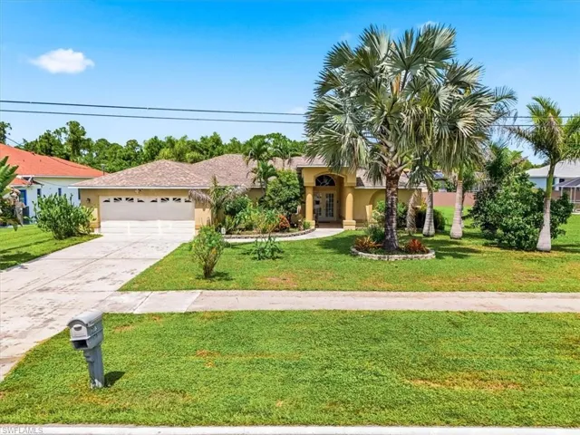 Single-story residence featuring a two-car garage, concrete driveway, and mature palm trees