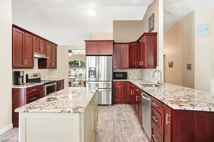 Kitchen with wood-finish flooring, rich wood cabinetry, stainless steel appliances, speckled stone countertops, and a central island