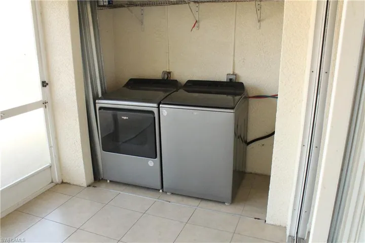 Laundry room with washer and clothes dryer, a textured wall, and light tile patterned flooring