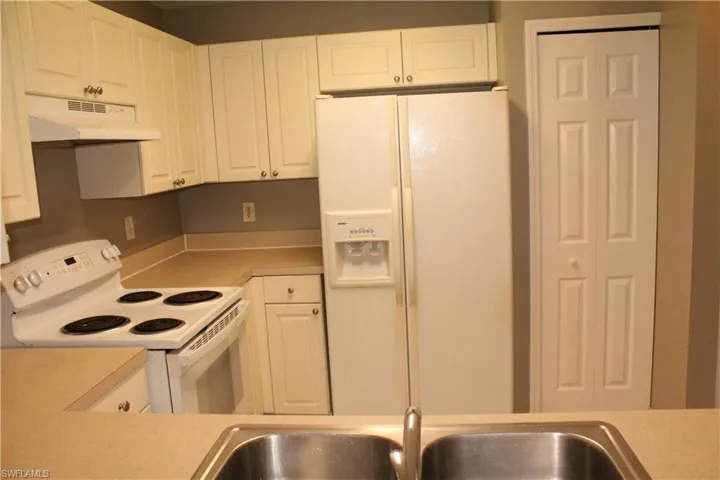 Kitchen with white appliances, light countertops, white cabinetry, and under cabinet range hood