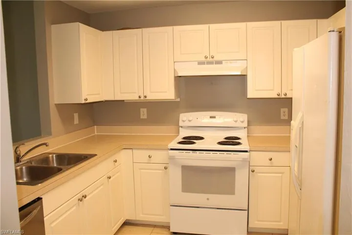 Kitchen with white appliances, light countertops, white cabinetry, and under cabinet range hood
