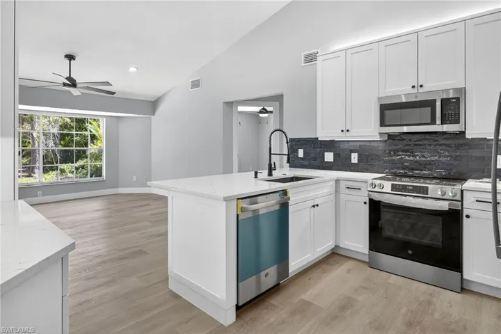 Kitchen featuring vaulted ceiling, stainless steel appliances, a ceiling fan, tasteful backsplash, and light wood-style floors