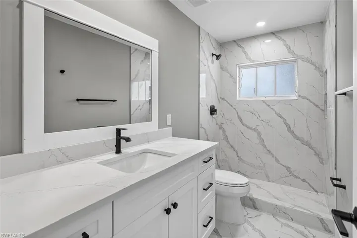 Guest bathroom featuring white wood vanity with Quartz top a marble look shower, and marble look floors,